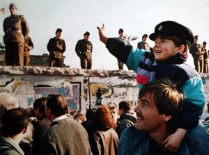 A boy waves to soldiers on the Berlin Wall in front of the Brandenburg Gate on November 10th, 1989. 