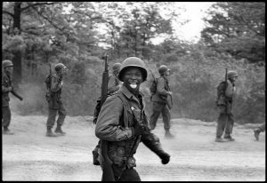 A marching soldier sticks his tongue out at the photographer, by Elliott Erwitt, Fort Dix, 1951. 