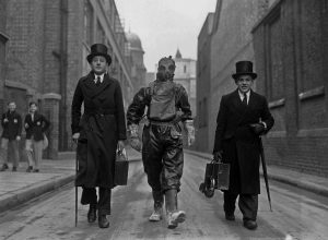 Boys being walked to school in Westminster by city employee with gas mask on. [1938] [Retouched] 