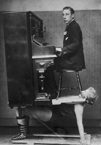 A circus strongwoman balances a piano and pianist on her chest, 1920s.