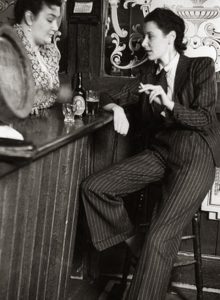 Anne Scott James in pinstripe suit sips beer and smokes at a pub, 1941.