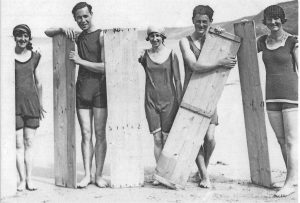 Riding waves in 1920s style - heavy, solid wood surfboards.