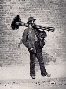 A chimney sweep strides with his bundle of brooms, London, 1884.